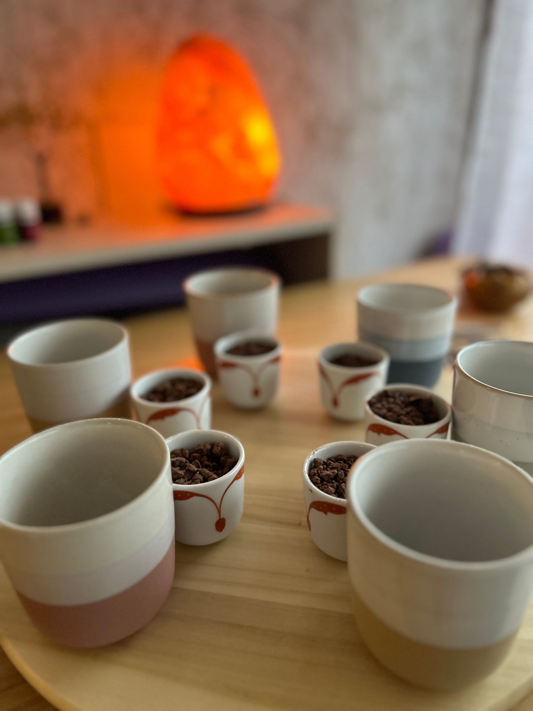 Tazas y cuencos con cacao preparados en círculo, con una lámpara de sal al fondo
